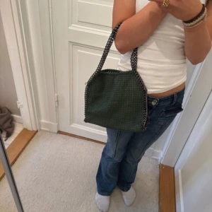 Grön axelväska med kedjedetaljer - Snygg grön axelväska med coola kedjedetaljer längs kanterna. Väskan har en stilren design och är perfekt för att ge din outfit en edgy touch. Den är rymlig nog för att bära dina dagliga nödvändigheter.