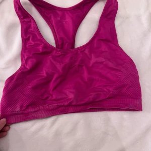 Rosa sport-bh från Champion - Säljer en rosa sport-bh från Champion i syntetmaterial. Den har en racerback-design och bred resår under bysten för extra stöd. Perfekt för träning och aktivitet.