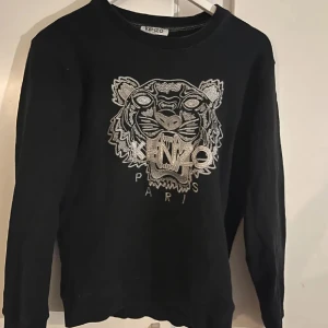 Svart sweatshirt från Kenzo - HELT NY Snygg svart sweatshirt från Kenzo med ett ikoniskt tigerhuvud och logotyp broderat i silver på framsidan. Tröjan har långa ärmar och en rund halsringning. Perfekt för en stilren look.