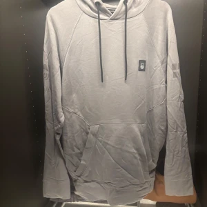 Grå hoodie från Sail Racing - Säljer en stilren grå hoodie från Sail Racing. Tröjan har en klassisk design med känguruficka och justerbar huva med snören. Perfekt för en avslappnad look.