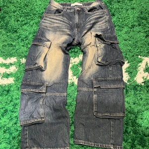 Blå cargopants från Bershka - Säljer ett par blå cargopants från Bershka med flera praktiska fickor och en avslappnad passform. Byxorna har en slitstark look med ljusa tvättade detaljer och knappar i midjan. Perfekta för en casual stil.