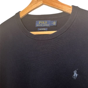 Mörkblå stickad tröja från Ralph Lauren - Säljer en stilren mörkblå tröja från Ralph Lauren i mycket fint material, 100% pima bomull. Tröjan har en klassisk design med långärmade ärmar och en liten broderad logotyp på bröstet. Perfekt för en avslappnad och elegant look. Storleken är M, men den skulle nog kunna passa en S också. Skicket är mycket bra, så gott som ny 