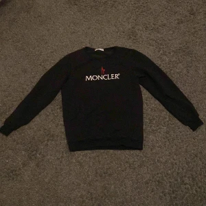 Svart tröja från Moncler - Snygg svart tröja från Moncler med deras ikoniska logga broderad på framsidan. Tröjan har långa ärmar och en klassisk passform. Perfekt för en stilren look. Passar 170cm