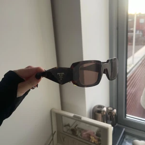 Solglasögon från Prada - Snygga solglasögon från Prada med en rektangulär form och trendigt sköldpaddsmönster. De har mörka linser och kommer med ett svart fodral. Välbehållna och sparsamt använda. Skicket är mycket bra🤎