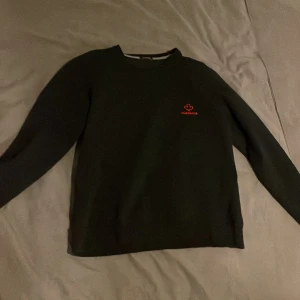 Svart tröja från Dsquared2 - Säljer en stilren svart tröja från Dsquared2 med röd broderad logotyp och lönnlöv på bröstet. Tröjan har långa ärmar och en klassisk passform. Perfekt för en avslappnad och trendig look.