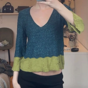 Blå och grön stickad tröja - Säljer en unik stickad tröja i blått och grönt med v-ringning. Tröjan har trekvartsärmar och en fin ribbad detalj vid ärmslut och nederkant. Perfekt för en avslappnad stil.