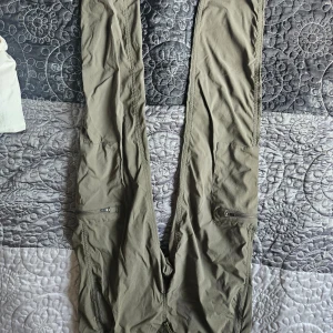 Gröna cargopants från The North Face - Säljer ett par khakifärgadd cargopants från The North Face. De är perfekta för utomhusaktiviteter med sina praktiska fickor och slitstarka material. Byxorna har en avslappnad passform och är idealiska för både vardag och äventyr.