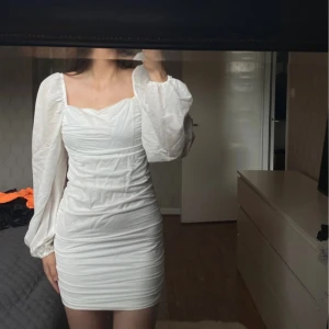 Vit kortklänning med puffärmar - Säljer en superfin vit kortklänning med puffiga långa ärmar. Klänningen har en tight passform och en dragkedja i ryggen. Perfekt för fest eller sommarens alla tillfällen! 💫 Endast använd 1 gång vid min student.