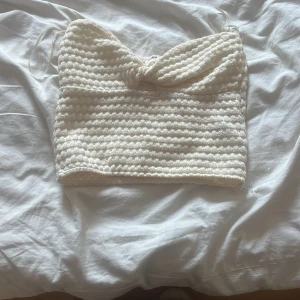 Vit stickad tubtopp - Säljer en superfin vit stickad tubtopp som är perfekt för sommaren. Den är ribbad och har en söt knutdetalj framtill. Toppen är ärmlös och passar perfekt till både fest och vardag. Den är i nyskick och redo att bäras av någon som älskar en stilren look!pris kan diskuteras !!!!