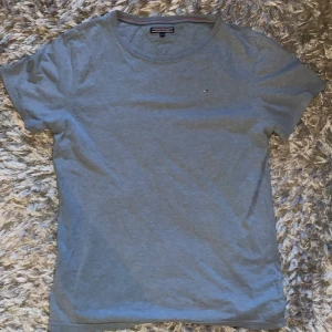 Tommy Hilfiger T-Shirt - Snygg ljusblå Tommy Hilfiger i storlek 176, passar som M. Riktigt skönt material och sparsamt använd, utan deffekter. Kan gå ner i pris vid snabbaffär.