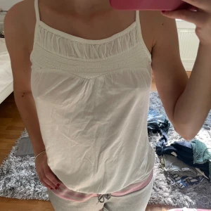 Vit ärmlös linnetopp - Säljer en enkel och stilren vit linnetopp. Den har smala axelband och en fin detalj upptill med små veck. Perfekt för sommardagar eller som ett basplagg i garderoben.