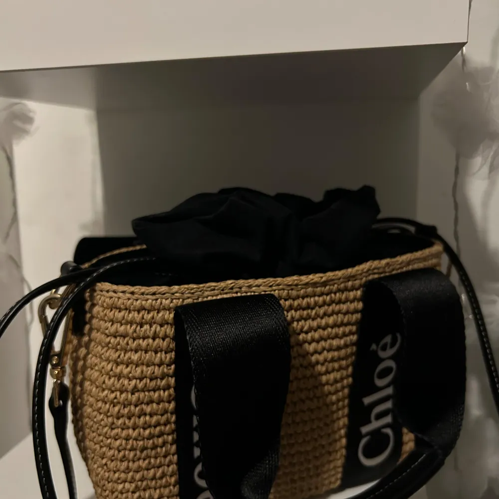 Säljer en superfin beige väska från Chloé. Den är gjord i ett flätat material som ger en snygg och somrig look. Väskan har svarta handtag med Chloé-loggan tryckt i vitt, vilket ger en cool kontrast. Perfekt för både vardag och fest!. Laukut & Käsilaukut.