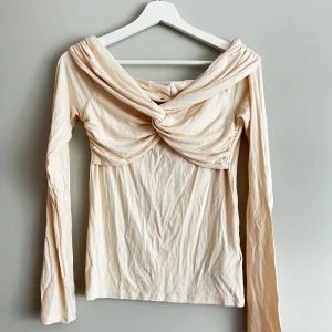 Beige långärmad topp med knutdetalj - Säljer en superfin beige långärmad topp med en unik knutdetalj framtill. Toppen har en offshoulder-stil. Oanvänd 