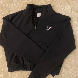 Svart croppad tröja från Gymshark - Säljer en svart croppad tröja från Gymshark med dragkedja och lång ärm. Perfekt för träning eller en avslappnad dag. Tröjan har en stilren design med Gymshark-logga på bröstet. Den är i väldigt bra skick och använd få gånger💓