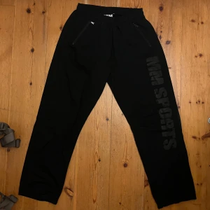 Svarta träningsbyxor från MM Sports - Svarta träningsbyxor från MM Sports med elastisk midja och dragkedja vid fickorna. Perfekta för gymmet eller en avslappnad dag. Modellen heter MM Hardcore Light Co Pants. Använda endast en fåtal gång då byxorna var för korta.