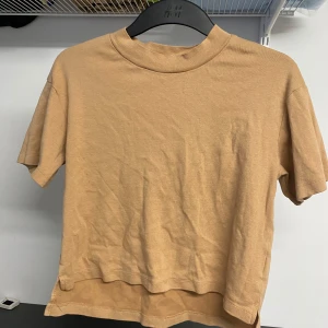 Brun t-shirt från Uniqlo - Säljer en beige t-shirt från Uniqlo. Den har en klassisk rund hals och korta ärmar, perfekt för en avslappnad look. Tillverkad i ett mjukt och bekvämt material.