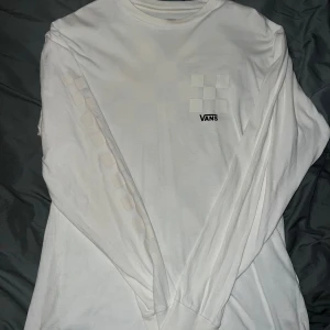 Vit långärmad tröja från Vans - Säljer en vit långärmad tröja från Vans i klassisk passform. Tröjan har ett subtilt rutmönster i beige/creme färg och Vans-logga på bröstet. Perfekt för en avslappnad stil.