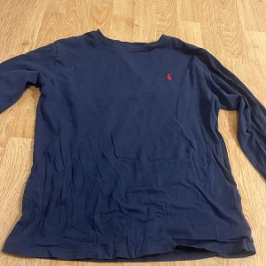 Mörkblå långärmad tröja från Ralph Lauren - Säljer en stilren mörkblå långärmad tröja från Ralph Lauren med en liten röd logotyp på bröstet. Perfekt för en avslappnad look. Tröjan är i storlek L och tillverkad i ett mjukt material.