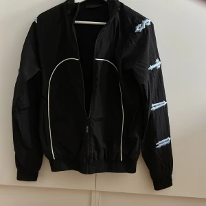 Svart jacka från Trapstar - Snygg svart jacka från Trapstar med  detaljer på ärmarna och dragkedja framtill. . Perfekt för en cool och avslappnad stil. 