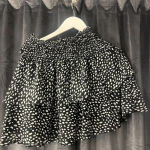 Svart och vit prickig kjol från Chelsea - Säljer en svart och vit prickig kjol från Chelsea med volanger. Kjolen har en elastisk midja för en bekväm passform och är perfekt för en trendig look.