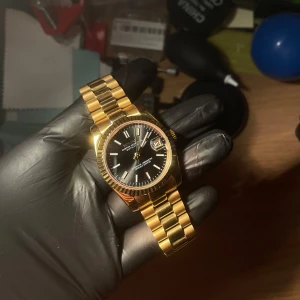 Seiko Datejust mod - Modiferad guldfärgad klocka med svart urtavla och datumvisning. Klockan har en klassisk länkarmband i guld och en tydlig urtavla med lysande visare. Perfekt för den som vill ha en tidlös och stilren accessoar. Storleken är 36mm och klockan är rostfritt stål.