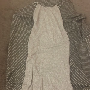 Grå ärmlös klänning - Säljer en stilren grå ärmlös klänning med smala axelband. Perfekt för en avslappnad look. Klänningen har en enkel design och är gjord i ett mjukt material.