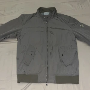 Grå bomberjacka från J.Lindeberg - Grå/Silvrig sällsynt bomberjacka av märket J.Lindeberg. Storlek L, men skulle nog säga att den passar M. Skicket bra, dock är det en liten bristning i vadderingen på en av ärmarna, dock något som inte syns vid användning. Priset är inte hugget och kan gå ned i pris vid snabb affär🙌 Kan lösa fler bilder.