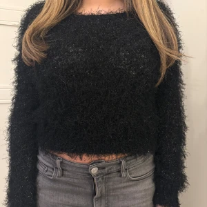Svart fluffig tröja - Säljer en svart fluffig tröja med glittrande detaljer. Tröjan är croppad och har långa ärmar, perfekt för en trendig look. Passar bra till både jeans och kjol. Perfekt för höst och vinter!
