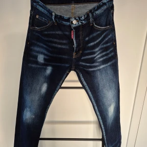 Mörkblå jeans med kanadensisk flagga - Snygga mörkblå jeans med slitna detaljer och en cool kanadensisk flagga på bakfickan. Jeansen har en klassisk femficksdesign och en knappgylf. Perfekta för en avslappnad stil med en touch av attityd. Regular fit