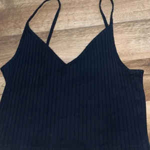 Svart ribbad linnetopp från H&M Divided - Säljer en svart ribbad linnetopp från H&M Divided. Toppen har smala axelband och en v-ringad design. 
