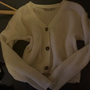 Vit kofta från 157 - Säljer en mysig vit kofta från 157 med knappar framtill. Perfekt för lager-på-lager och passar till många olika outfits. Koftan har en ribbad struktur och långa ärmar.