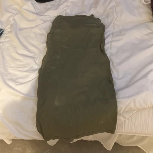 Olivgrön axelbandslös klänning - Snygg olivgrön axelbandslös klänning i ett mjukt och följsamt material. Perfekt för en stilren och enkel look. Passar bra till både vardag och festliga tillfällen.