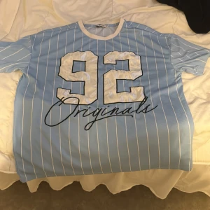 Blå och vit randig t-shirt med tryck - Snygg blå t-shirt med vita ränder och trycket '92 Originals' i svart. Perfekt för en avslappnad stil.