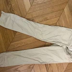 Beige chinos från Polo Ralph Lauren - Snygga beige chinos från Polo Ralph Lauren med dragkedja och knappar. Perfekta för en stilren look. De har praktiska fickor och bälteshällor för extra funktionalitet.