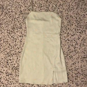 Ljusgrön blommig klänning från Bik Bok - Ganska kort ljsugrön klänning med mönster av små rosor. Smala axelband och liten slits nedtill på framsidan. Svalt glansigt tyg. 