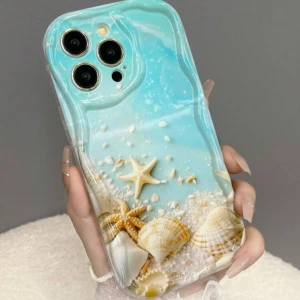 Mobilskal med strandmotiv - iPhone 15 - Snyggt mobilskal med ett strandmotiv som inkluderar snäckor och en sjöstjärna. Skalet har en blå bakgrund som ger en somrig känsla. Perfekt för att ge din telefon ett unikt och fräscht utseende.