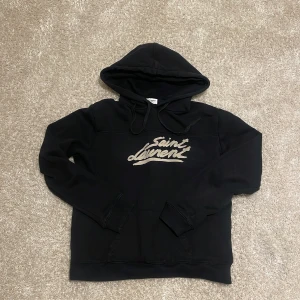 Saint Laurent hoodie - Snygg svart hoodie från Saint Laurent med deras ikoniska logga i beige på bröstet. Hoodien har inga defekter och är i bra skick. Storlek S. Mvh store 101