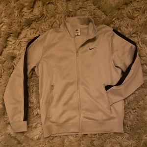 Nike träningsjacka  - Snygg beige träningsjacka från Nike. Nike-logga både fram och bak. Köpt i Spanien i Nike affär för ca 900kr, och endast använda ett par gånger. Kan användas både som jacka och vardaglig tröja. Står M på tröjan men passar L.