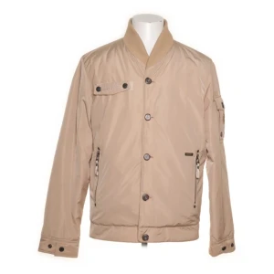 Beige jacka från Wiggy's - Snygg beige varma jacka från Wiggy's med knappar och dragkedja i fickorna. Jackan har en hög krage och flera praktiska fickor. Perfekt för kyligare dagar med sin quiltade insida. Jackan är mycket gott skick och original lapparna kvar. Har använts i ett fåtal gånger och kommer från ett djur- och rökfritt hem.