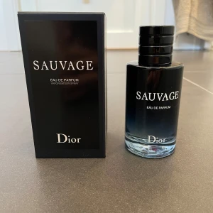 Sauvage Eau de Parfum från Dior - Säljer en flaska Sauvage Eau de Parfum från Dior. Flaskan har en elegant design med en mörk toning och svart lock. Parfymen är känd för sin fräscha och maskulina doftprofil. Perfekt för den som vill ha en tidlös och sofistikerad doft.