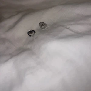 Silverfärgade hjärtformade örhängen - Söta och stilrena örhängen i form av hjärtan. Perfekta för att ge en subtil touch av elegans till din outfit. De är små och diskreta, vilket gör dem lätta att bära varje dag.