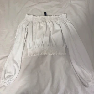 Vit offshoulder topp - Säljer en superfin vit offshoulder topp med långa ärmar. Den har en elastisk smockdetalj vid axlar och midja som ger en snygg passform. Perfekt för sommarens alla fester eller en dag på stan. 🕊️