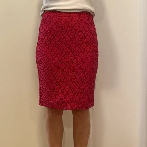 Röd/rosa kjol från Esprit - Snygg röd kjol från Esprit med ett coolt blommigt mönster. Kjolen är i en tight passform och perfekt för både fest och vardag. Den har en dragkedja baktill för enkel påklädning. Materialet känns lyxigt och bekvämt, vilket gör den idealisk för höst och vår.