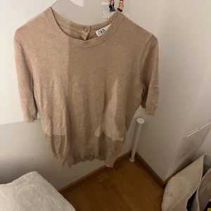 Beige tröja från Zara - Säljer en snygg beige tröja från Zara i storlek S. Den har trekvartsärmar och knappar i ryggen. Tröjan är använd, men fortfarande i bra skick!