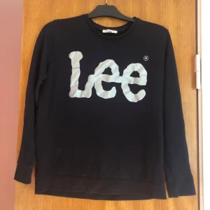 Svart tröja från Lee - Säljer en svart tröja från Lee i storlek M. Den har ett stort, vitt Lee-tryck på framsidan och är gjord i ett mjukt material. Perfekt för en avslappnad stil och passar bra till både jeans och joggers. Tröjan har långa ärmar och en klassisk rund halsringning. Lite nopprig, se bild