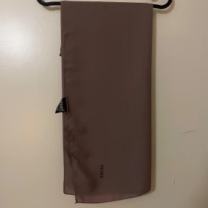 Beige sjal från Sedef - Säljer en elegant beige sjal från Sedef. Den är i nyskick. Materialet är chiffon. Passar bra till höst och vår. Helt ny och oanvänd. Undercapen är ihopsatt med sjalen.