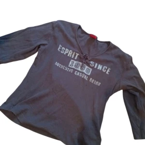Grå tröja från Esprit - Säljer en grå tröja från Esprit med texten 'Esprit Since 1968' på framsidan. Tröjan har en v-ringad hals med knytning och trekvartsärmar.