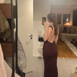 Mörk vinröd långklänning med öppen rygg - Säljer en elegant mörk vinröd långklänning med en fantastisk öppen rygg. Klänningen är tight och perfekt för festliga tillfällen. Den är ärmlös och har en stilren design som framhäver figuren. Perfekt för en kväll ute eller en speciell tillställning.