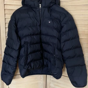 Gant vinterjacka pojke - Fin blå vinterjacka, sparsamt använd, inget synligt slitage, fickor med tryckknapp, innerficka. Det står 170 och 15 år i jackan, men liten i storleken, min son är 172 och 14 år och den är för liten. 