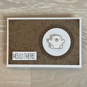 Handgjort kort med björnmotiv - Ett supergulligt handgjort kort med ett björnmotiv och texten 'Hello There'. Kortet har en brun bakgrund med små björnar och hjärtan, och en upphöjd björn i mitten. Perfekt för att skicka en hälsning till någon speciell! Kortet är vitt på insidan och har en personlig touch med en handritad katt på baksidan.